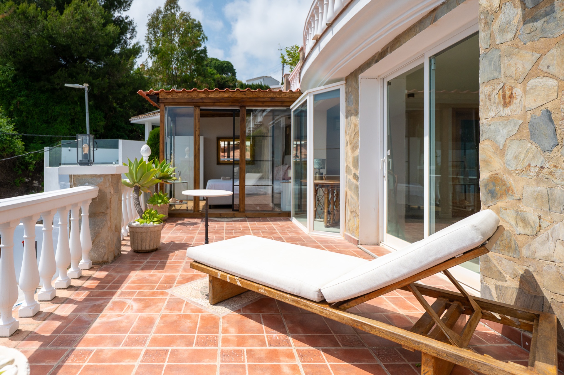 Zonnig terras met houten ligbed naast de serre met slaapkamer